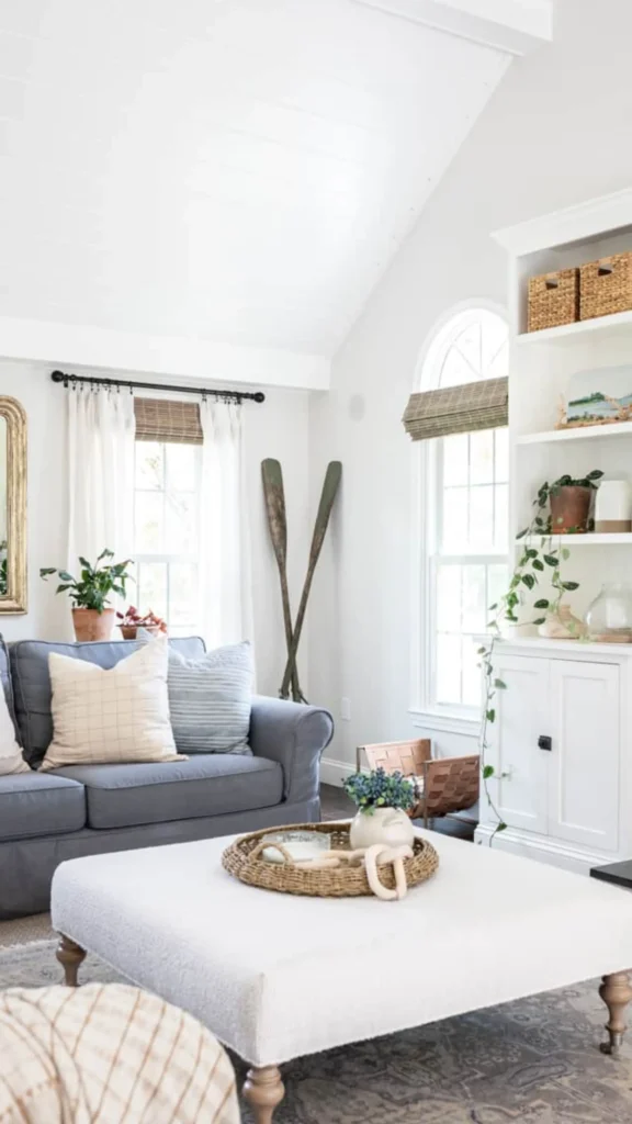 Modern farmhouse style summer home decor with a grey sofa, white beadboard ceiling, a large built-in bookshelf, and decorative wooden oars.