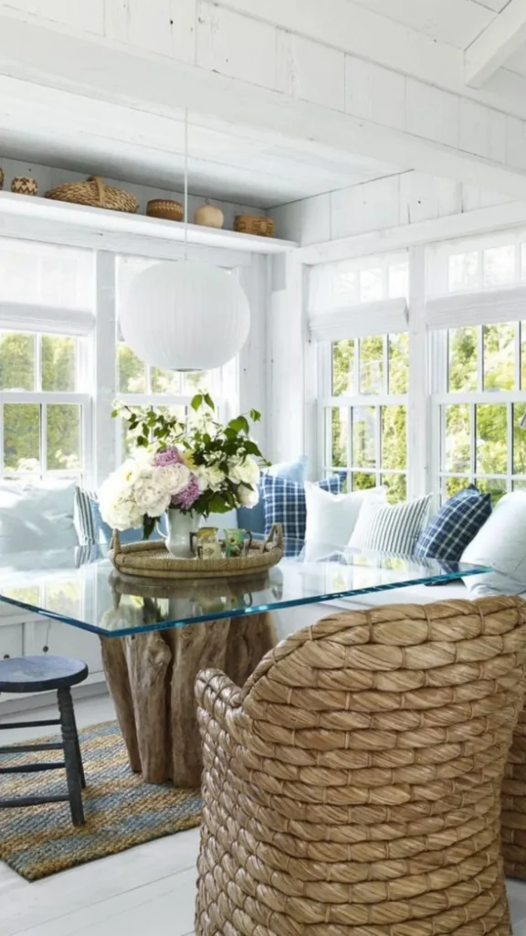 Rustic beach house summer home decor featuring a glass-top dining table with a driftwood base and heavy woven wicker chairs.