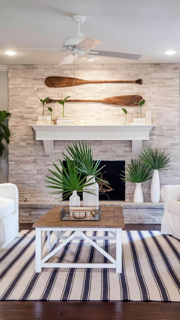 Coastal living room with white stone fireplace, wood oars wall decor, and a striped rug offering refreshing home decor ideas.
