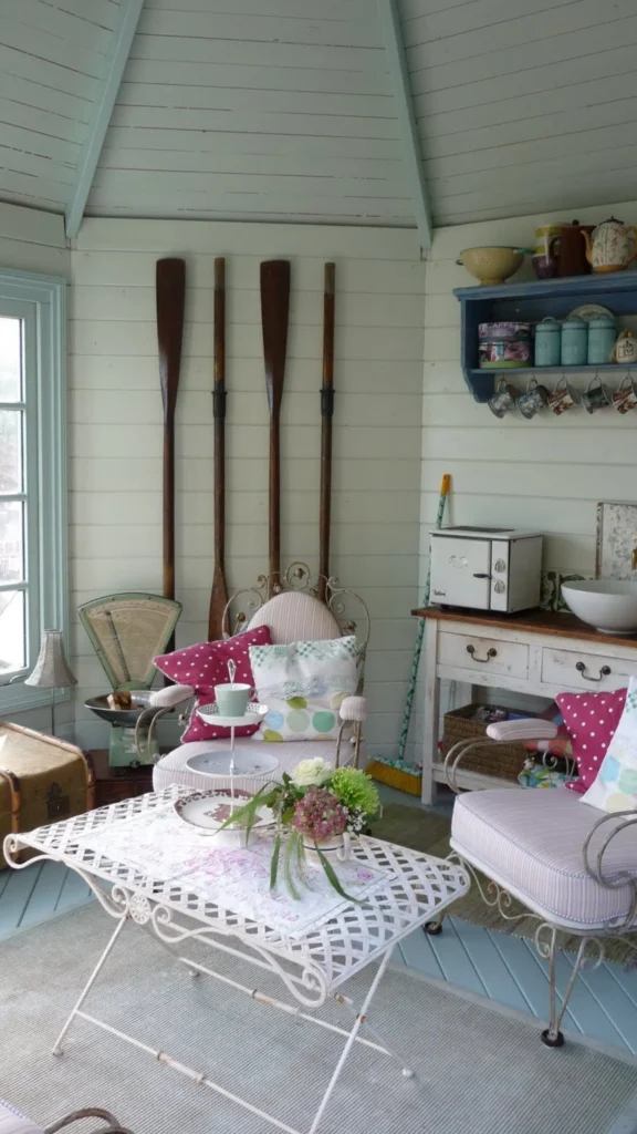 Charming vintage style summer home decor inside a wooden cottage with pastel blue trim, metal armchairs, and decorative wooden oars on the wall.