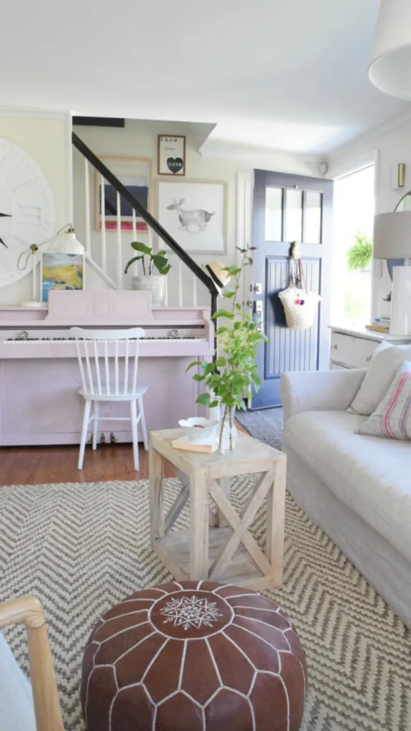 Whimsical summer home decor in a family room featuring a light pink upright piano, a chevron jute rug, and a brown leather pouf.