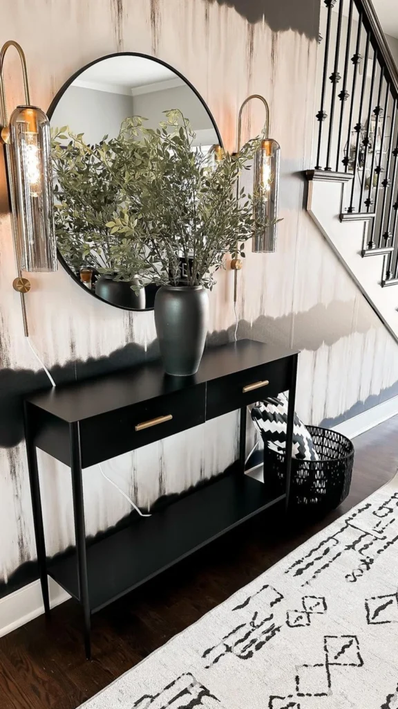 Modern contemporary entryway featuring a black console table, a large round mirror, glass tube wall sconces, and dramatic black and white watercolor wallpaper.