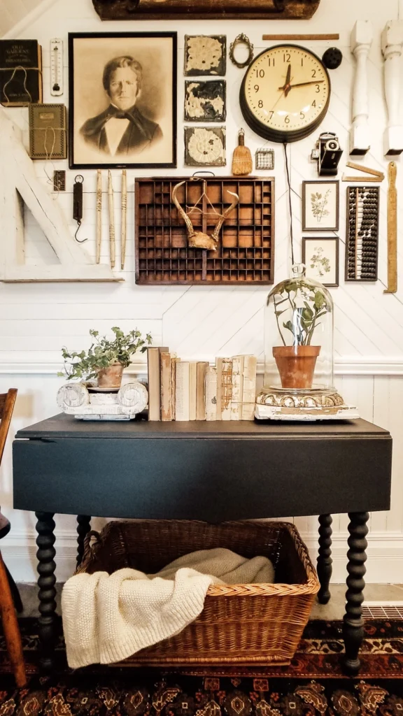 Curated rustic wall layout showcasing vintage home decor with antique tools, a vintage clock, antlers in a shadow box, and a black painted table.
