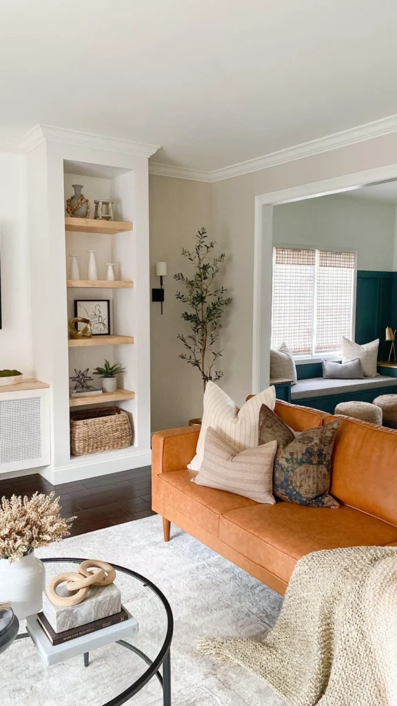 Transitional style small apartment decor featuring a tan leather sofa, built-in bookshelves, and a separate teal blue window seat nook.
