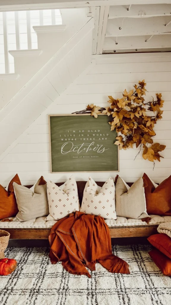 Under-stairs entryway bench displaying fall home decor ideas with a chalkboard October sign, fall leaf wreath, and rust-orange throw pillows.