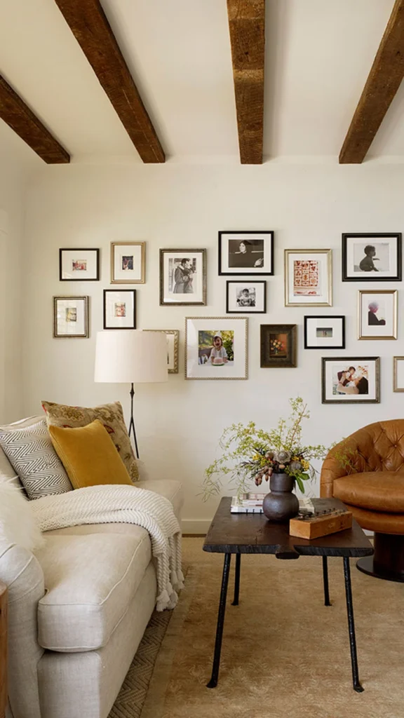 Bright living room with rustic home decor featuring exposed wooden ceiling beams, a large black-and-white frame gallery wall, and a tufted leather armchair.
