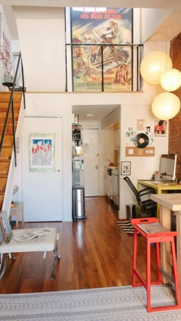 Industrial style open-plan layout for small apartment decor in a loft with wooden stairs, hanging paper globe lights, and a brick accent wall.