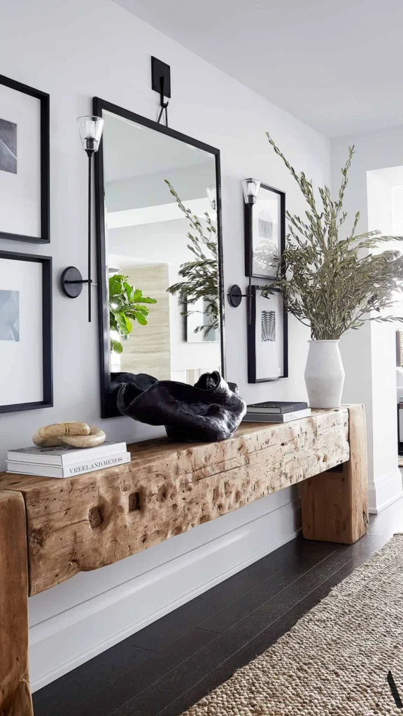Organic modern style entryway decor featuring a live-edge wooden console table, a large black-framed rectangle mirror, monochrome wall art, and a woven rug.