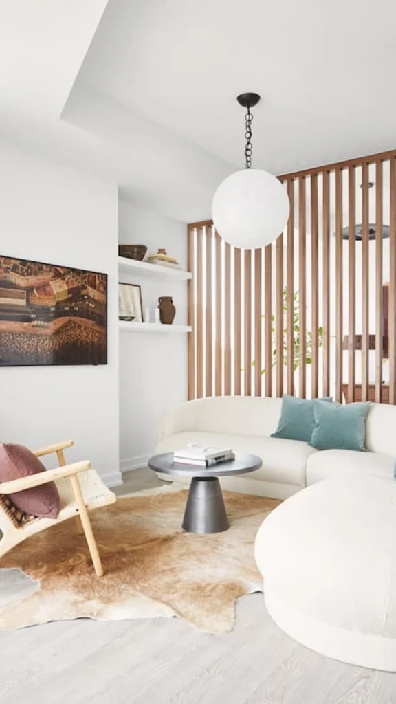 Chic organic modern small apartment decor with a curved white couch, blue velvet pillows, a cowhide rug, and a wooden slat divider screen.
