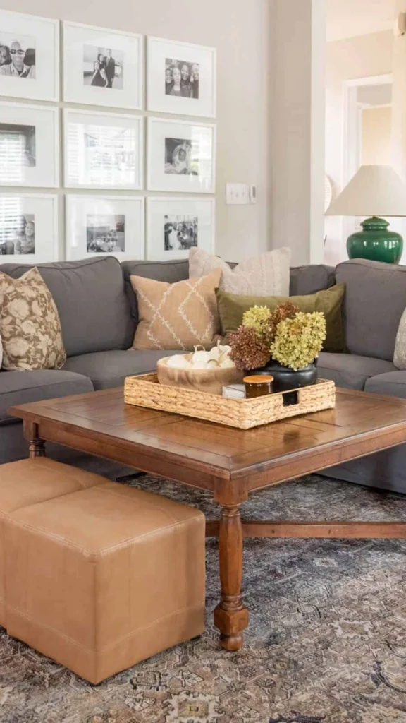 Modern living room featuring fall home decor ideas with a gallery photo wall, gray sectional sofa, and a woven coffee table tray with white pumpkins and dried flowers.
