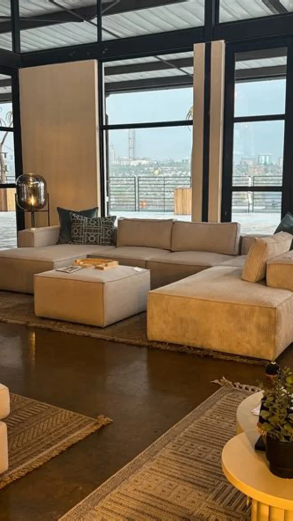 Spacious open-plan living room featuring lived in luxury with a large beige modular sectional sofa, oversized windows, and polished concrete floors.