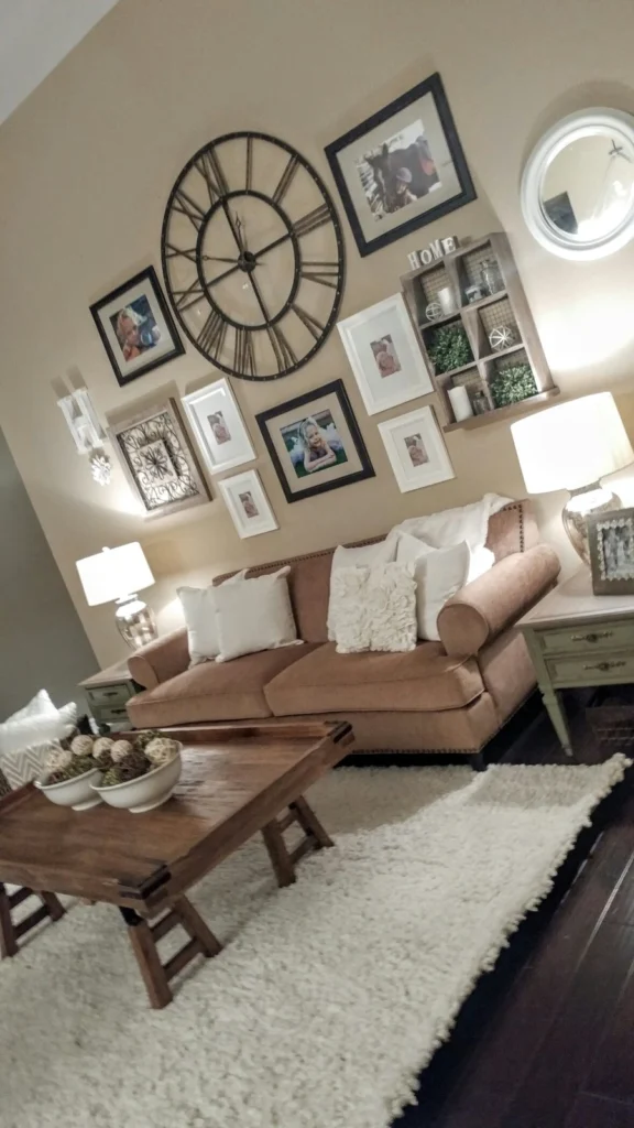 Cozy living room with wall decor ideas featuring a large metal Roman numeral clock, framed family photos, a brown sofa, and a wooden coffee table.
