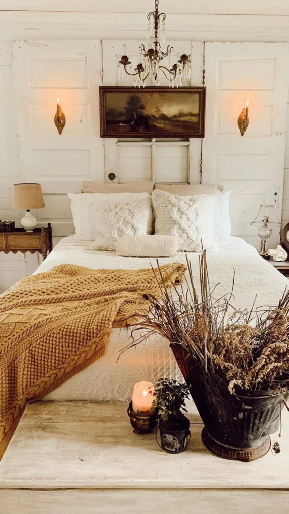 Rustic farmhouse bedroom showing vintage home decor with old wooden doors as a headboard, a white bed, a mustard yellow knit throw, and a crystal chandelier.