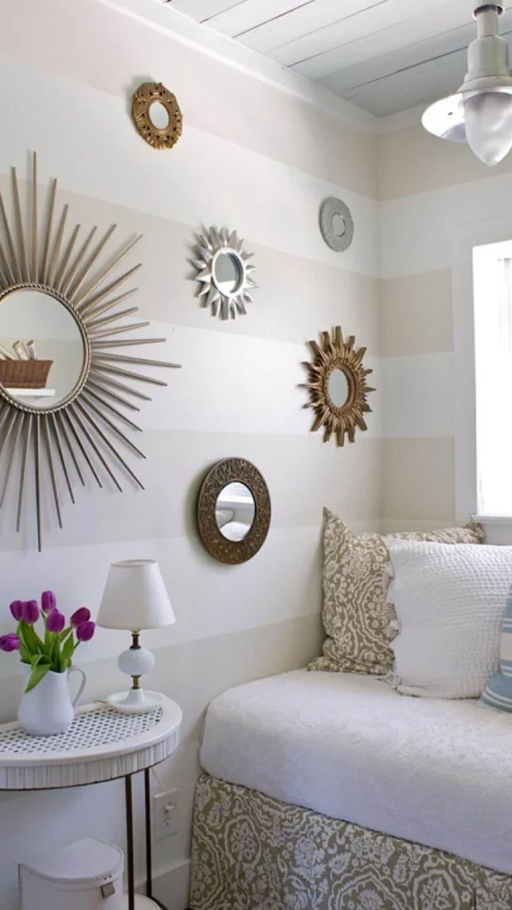 Cozy daybed nook displaying wall decor ideas with a collection of metallic sunburst and brass mirrors on striped wallpaper.
