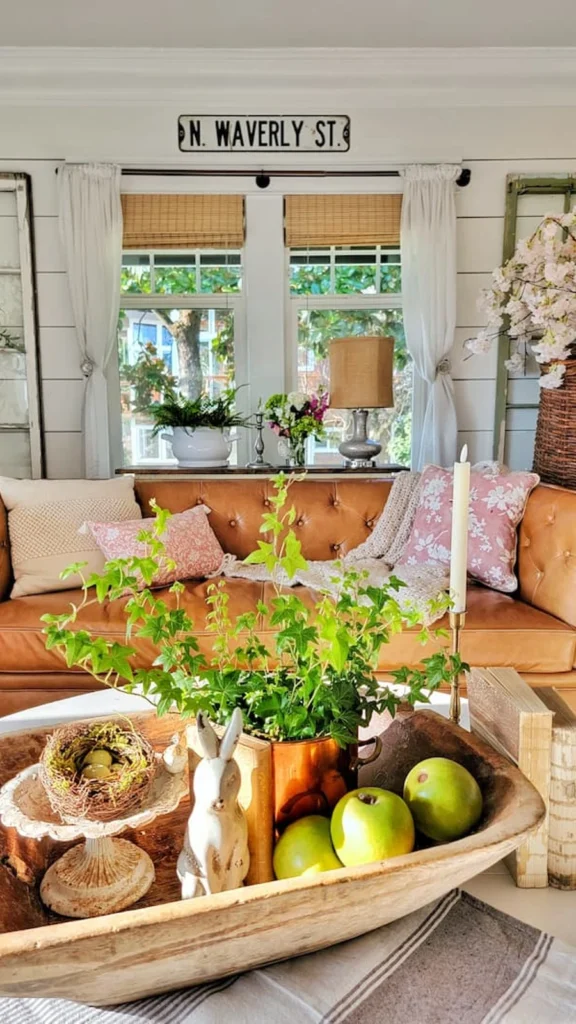 Cozy farmhouse living room displaying vintage home decor with a white sectional sofa, a wooden chest coffee table, a tall wood cabinet, and green ferns.