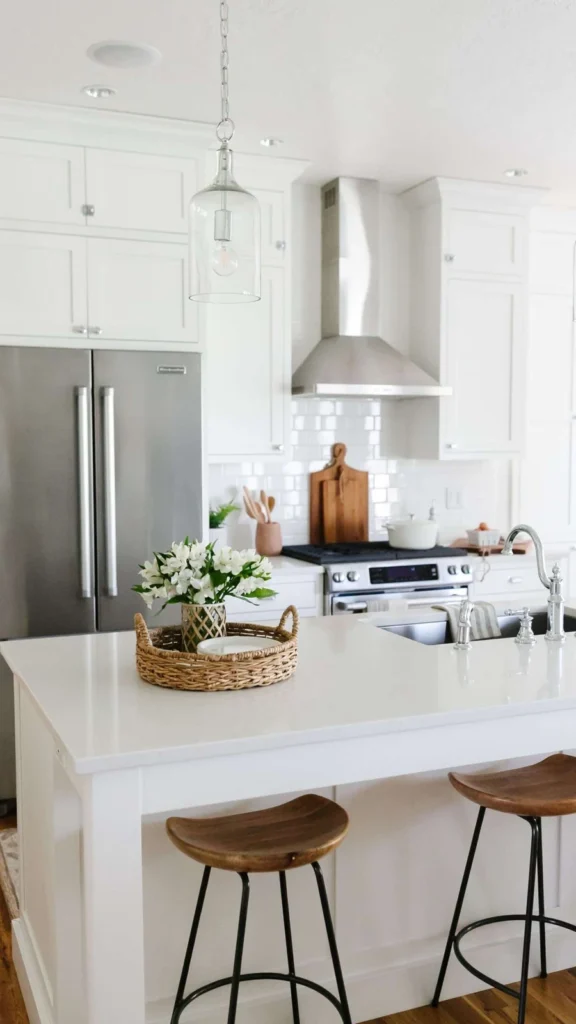 Crisp white kitchen featuring kitchen decorating ideas with a quartz island, wooden barstools, glass pendant lights, and stainless steel appliances.