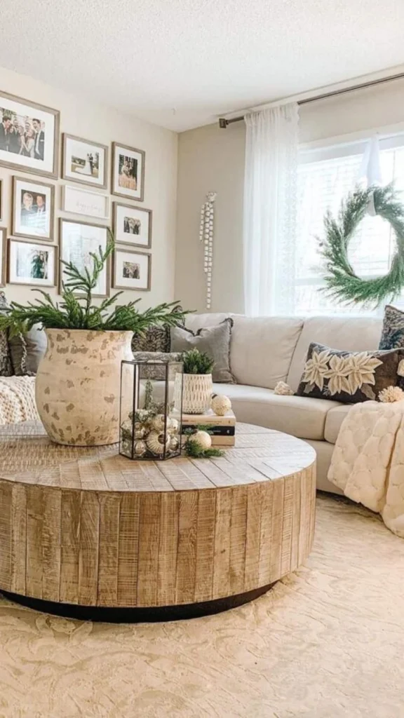 Cozy holiday living room displaying round coffee tables with a large distressed wood block drum table, an oversized vase, and a gallery wall