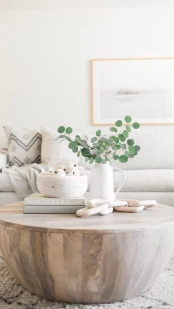 Bright minimalist room displaying round coffee tables with a solid light wood drum table, decorative wooden links, and a white sofa.